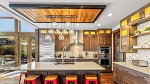 A modern kitchen with a large island, wooden cabinets, and red bar stools.