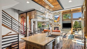 A modern kitchen with a central island, wooden flooring, and a stone fireplace.