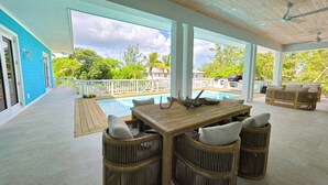 A covered outdoor area with a pool, wooden furniture, and a view of the surrounding greenery.