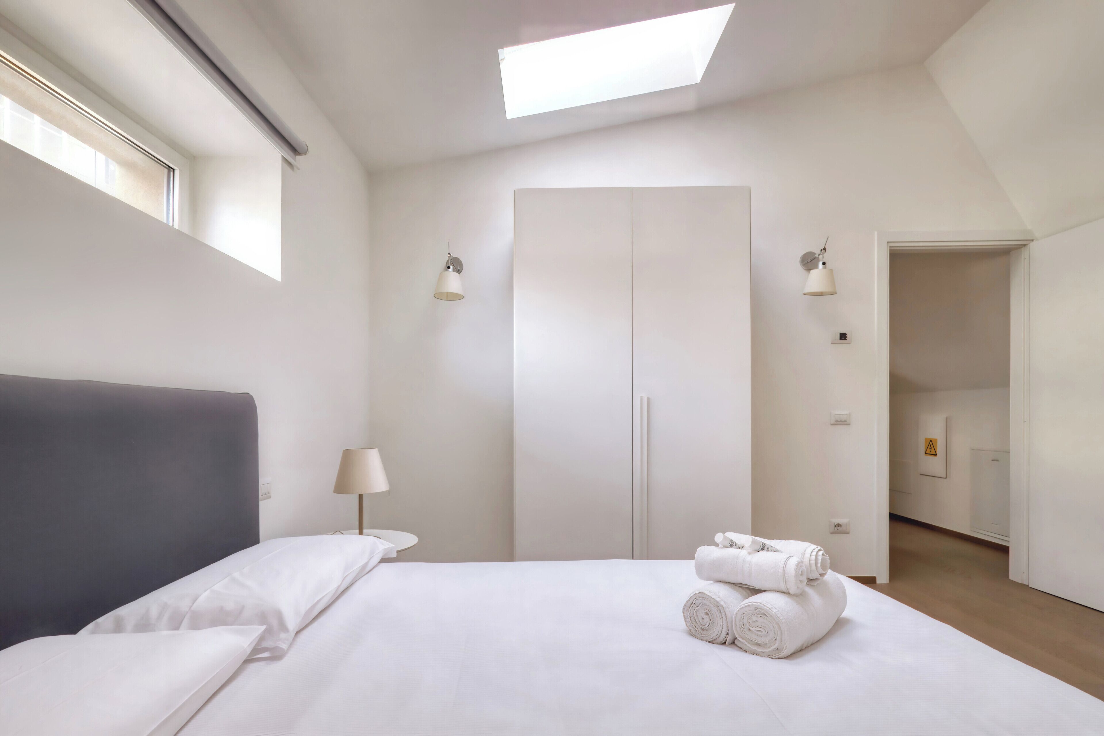Une chambre d’hôtel moderne dotée d’un grand lit, d’une lucarne, d’une armoire et d’une salle de bain visible à travers une porte ouverte.