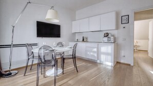 Una cucina moderna con mobili bianchi, una TV a schermo piatto e un'area pranzo con sedie trasparenti e un tavolo rotondo.