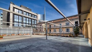 Una terrazza esterna con un edificio moderno sullo sfondo, una struttura metallica e piante in vaso.