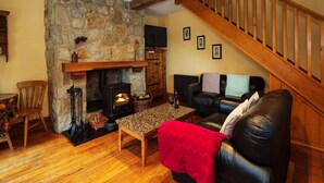 A cozy living room with a stone fireplace, a wooden staircase, and a leather sofa. - Charming 1-bedroom cottage in Rathdrum with WiFi (Rathdrum)