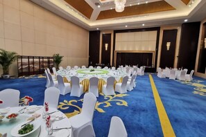 Un amplio salón de conferencias con mesas redondas, sillas blancas y una alfombra azul.