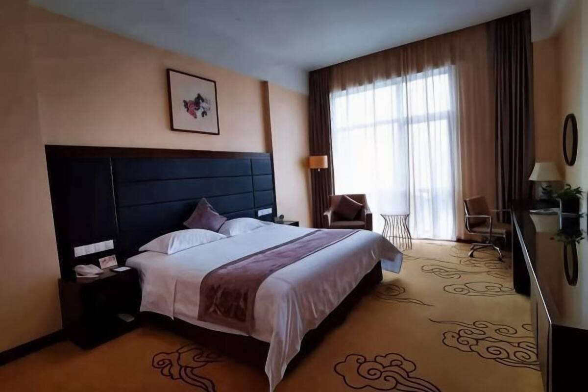A hotel room with a bed, nightstand, chair, desk, lamp, and curtains.