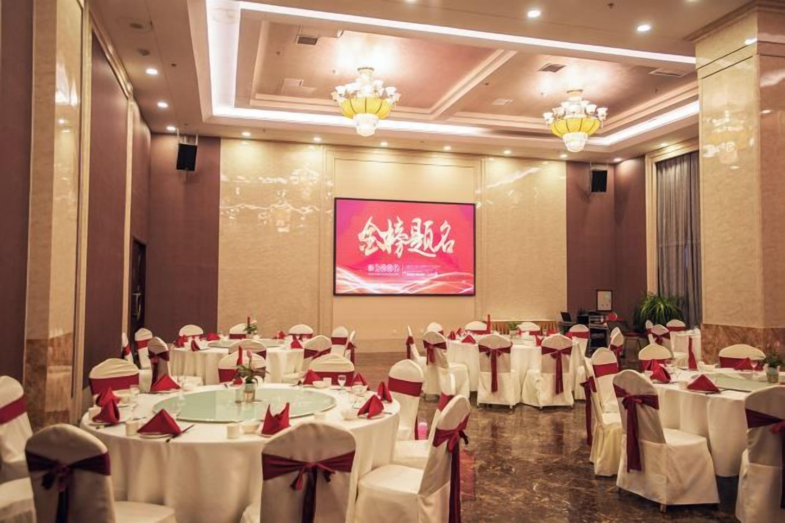 Un salón de banquetes con mesas redondas, manteles blancos y cintas rojas.