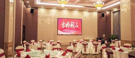 A banquet hall with round tables, white tablecloths, and red sashes.