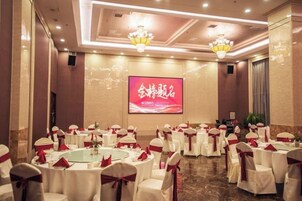 Un salón de banquetes con mesas redondas, manteles blancos y cintas rojas.
