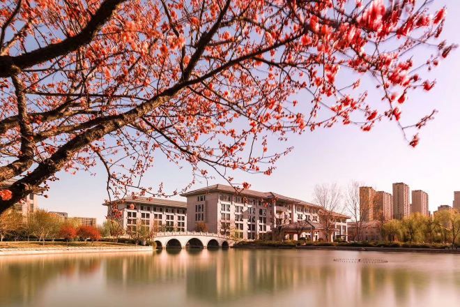 A hotel with a bridge over a calm body of water, surrounded by autumn foliage and modern buildings in the background.