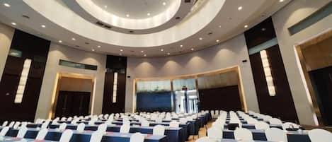 Un salón de conferencias con filas de mesas y sillas, un diseño de techo circular y un amplio ventanal.