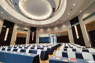 Un salón de conferencias con filas de mesas y sillas, un diseño de techo circular y un amplio ventanal.