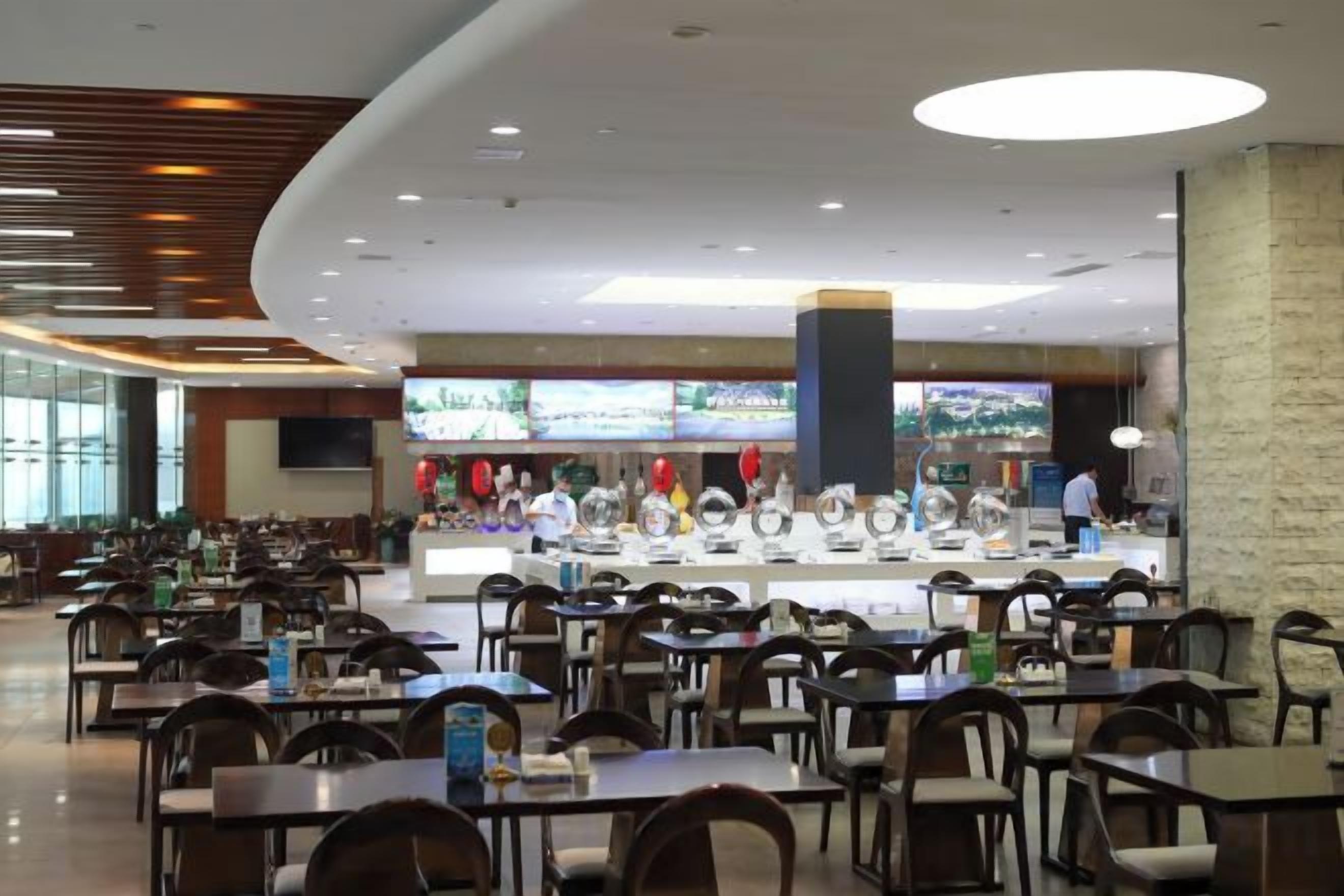 Un amplio comedor interior con varias mesas y sillas, una barra central con un televisor y un diseño de techo moderno.