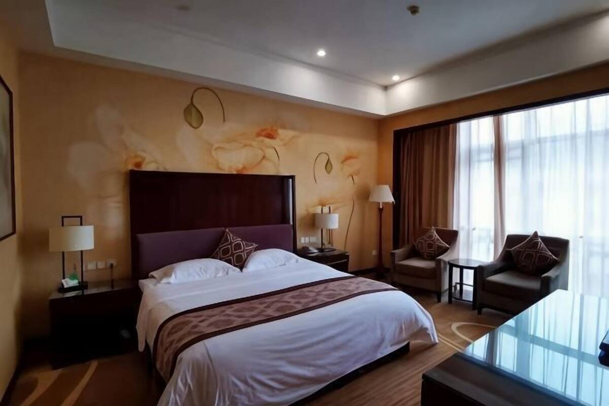 A hotel room with a large bed, a desk, two chairs, a glass table, and a view of the outdoors.