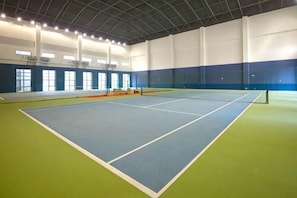 Een overdekte tennisbaan met een groen en blauw vloeroppervlak, witte wanden en een hoge plafond.