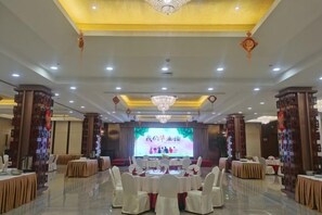 A banquet hall with round tables, chandeliers, and a stage. - Qisheng Internation Hotel (Zibo)