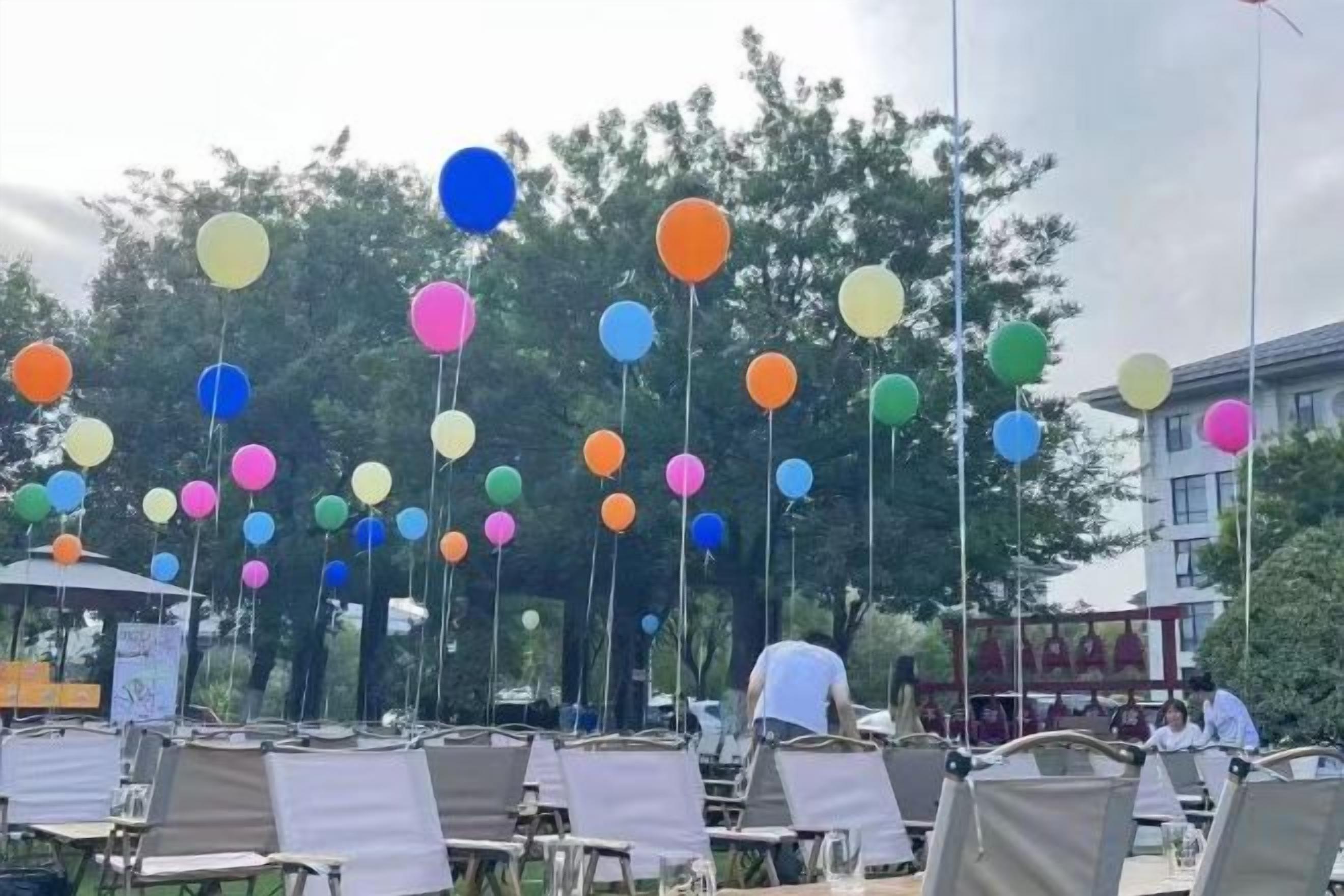 An outdoor seating area with multiple tables and chairs, and colorful balloons hanging from the ceiling.