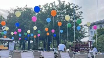 An outdoor seating area with multiple tables and chairs, and colorful balloons hanging from the ceiling.