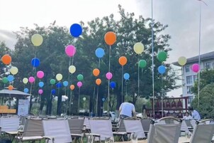 Un área de estar al aire libre con varias mesas y sillas, y globos de colores colgando del techo.