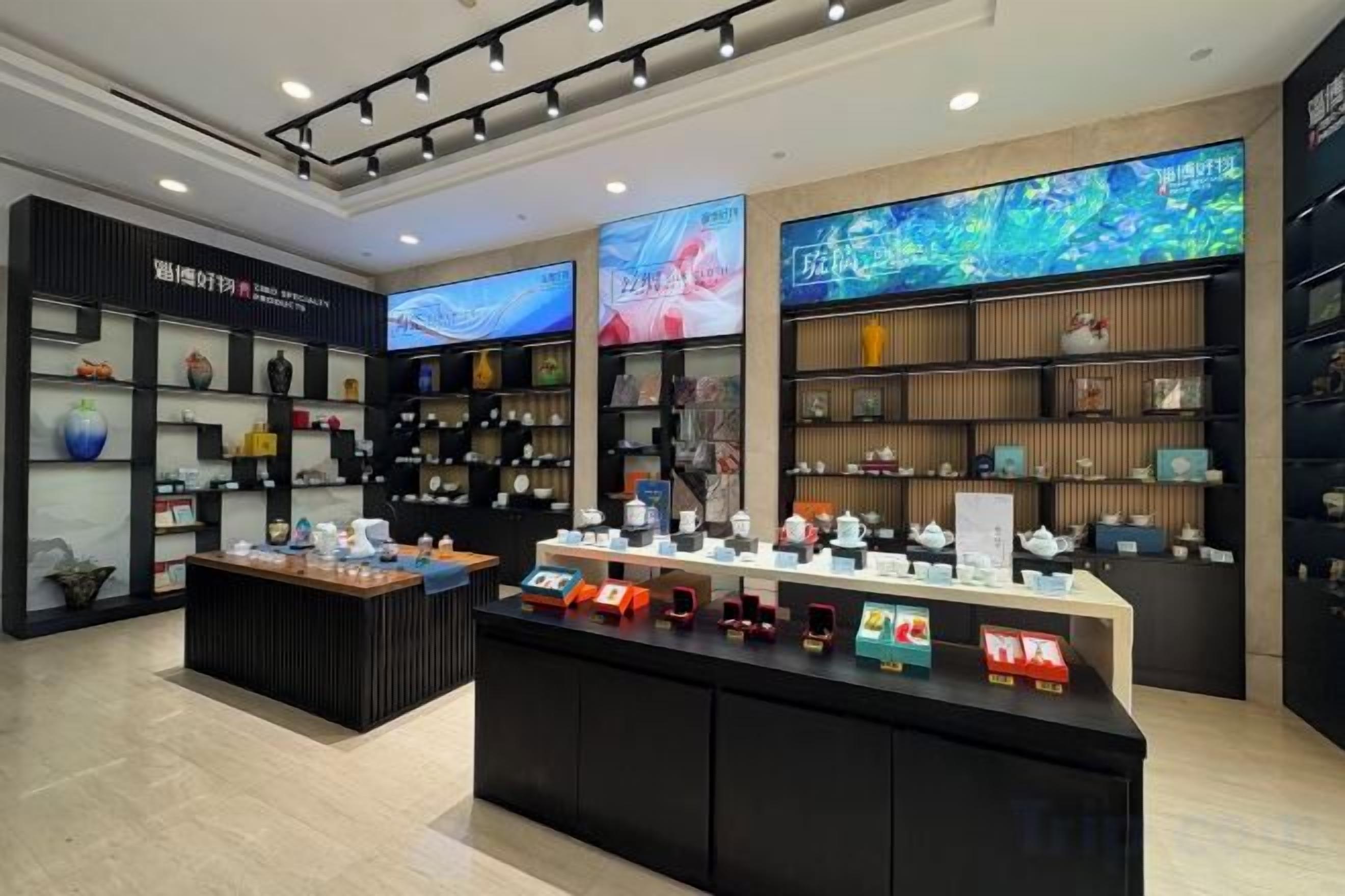 A retail store with shelves of products, a central display counter, and digital screens on the walls.