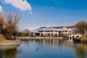 A building with a large pond in front, a bridge, and leafless trees. - Qisheng Internation Hotel (Zibo)