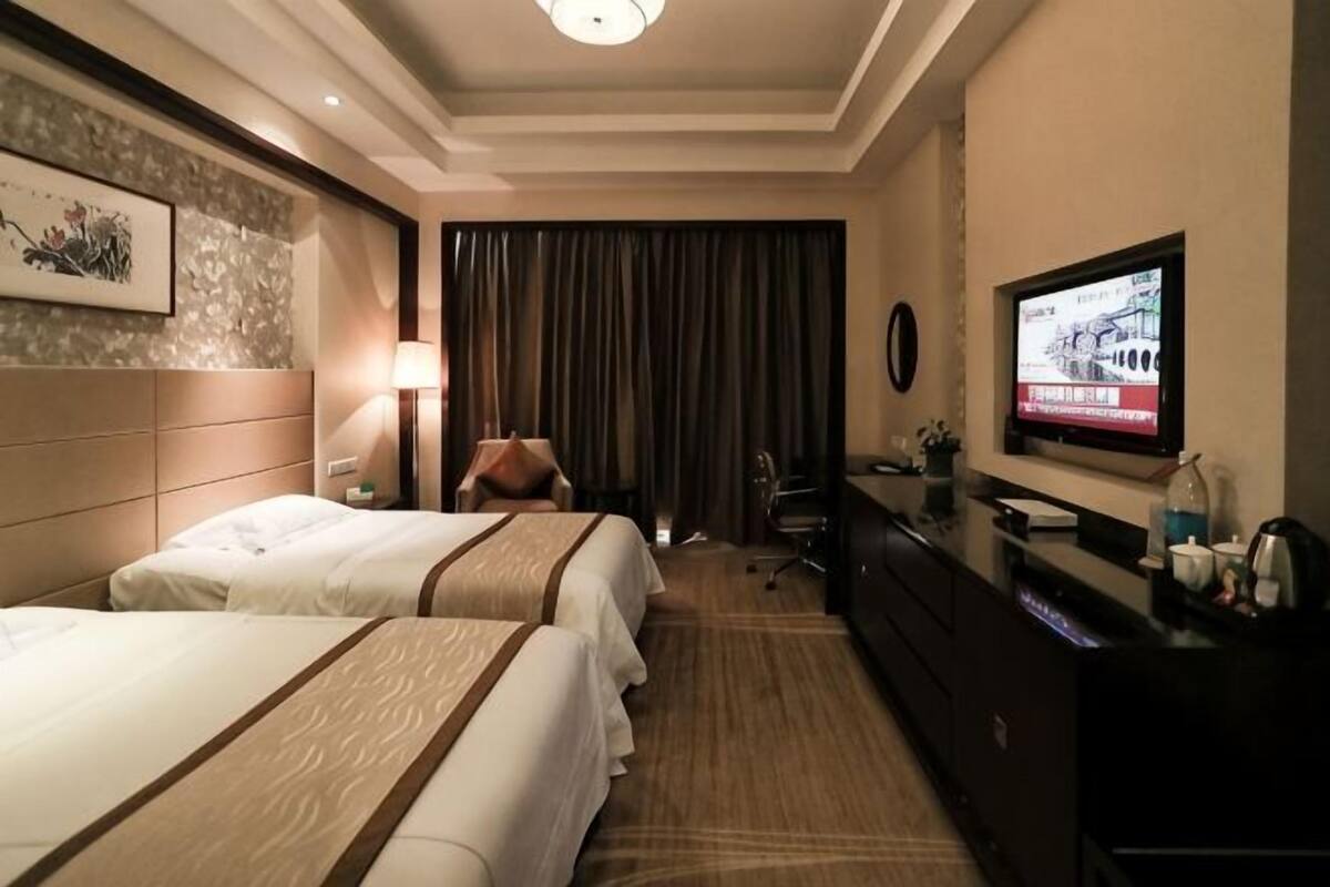 A hotel room with two beds, a desk, a TV, and a large window with curtains.