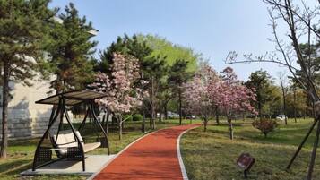 A park pathway with a swing set and a bench, surrounded by trees and a red path.