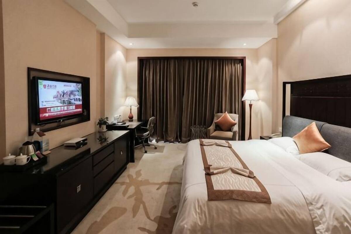 A hotel room with a bed, a desk, a television, a chair, and a window with curtains.