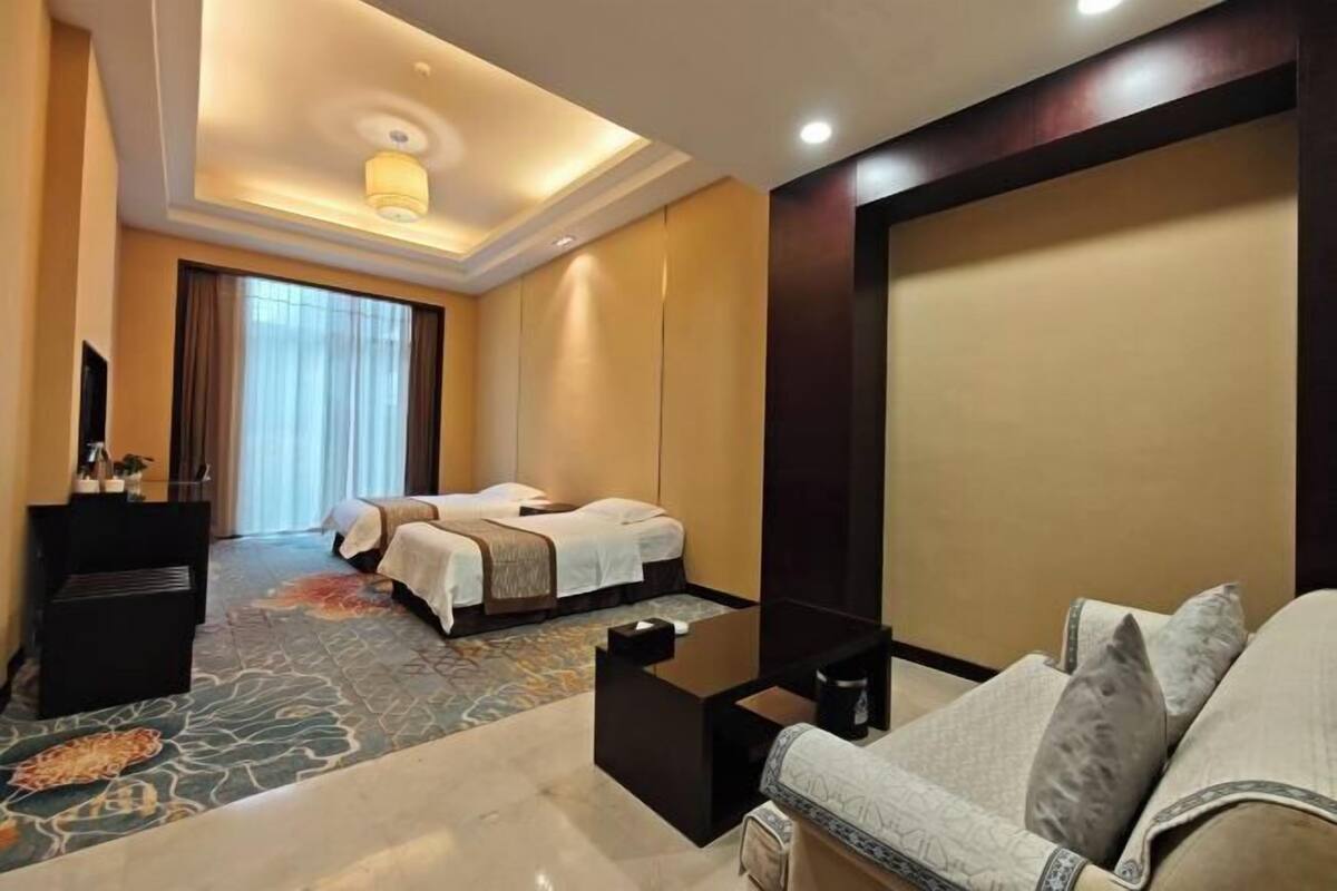 A hotel room with a bed, a sofa, a small table, a TV, and a large window.