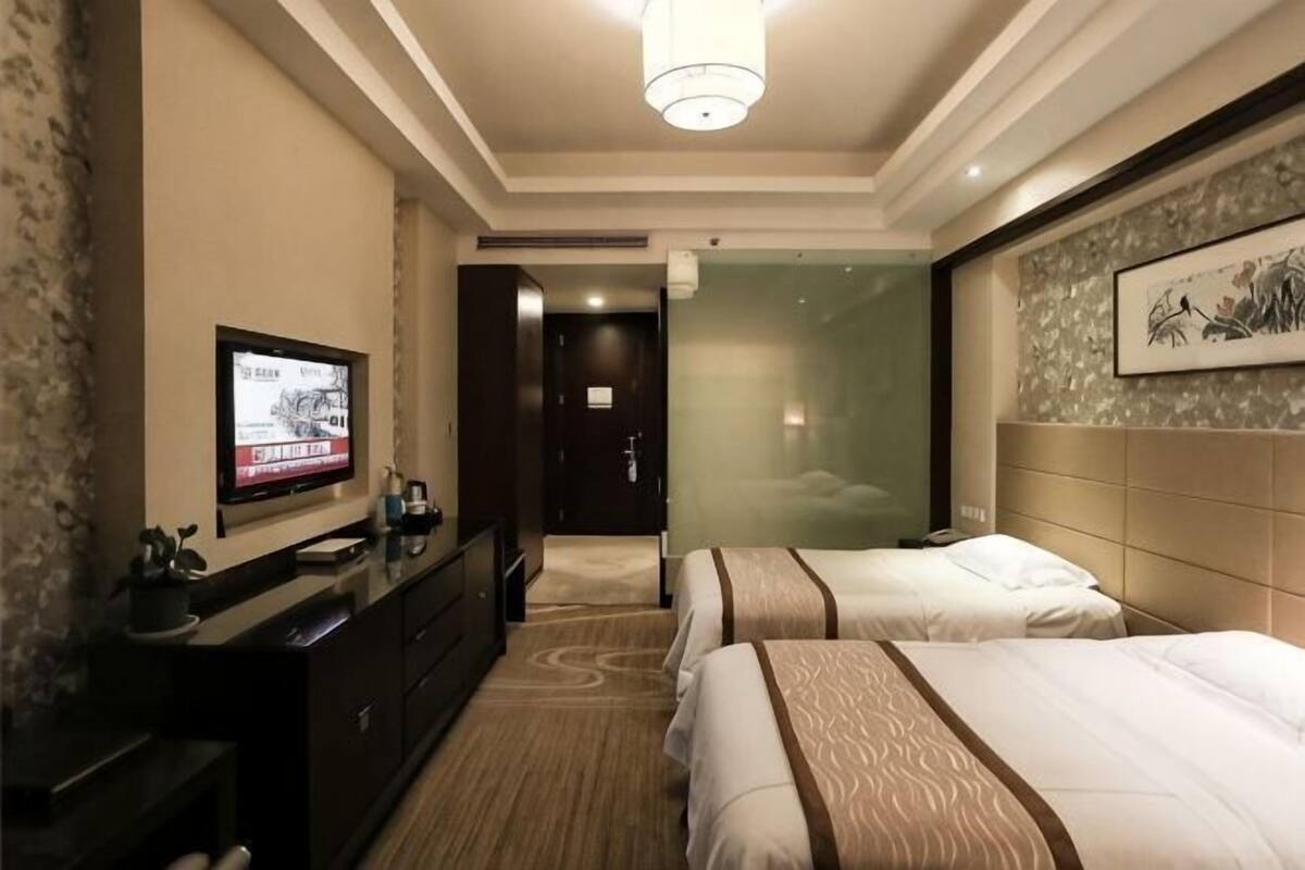 A hotel room with two beds, a TV, a dresser, and a door leading to another room.