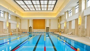 An indoor swimming pool with clear lanes, a tiled floor, and a high ceiling with a skylight. - Qisheng Internation Hotel (Zibo)