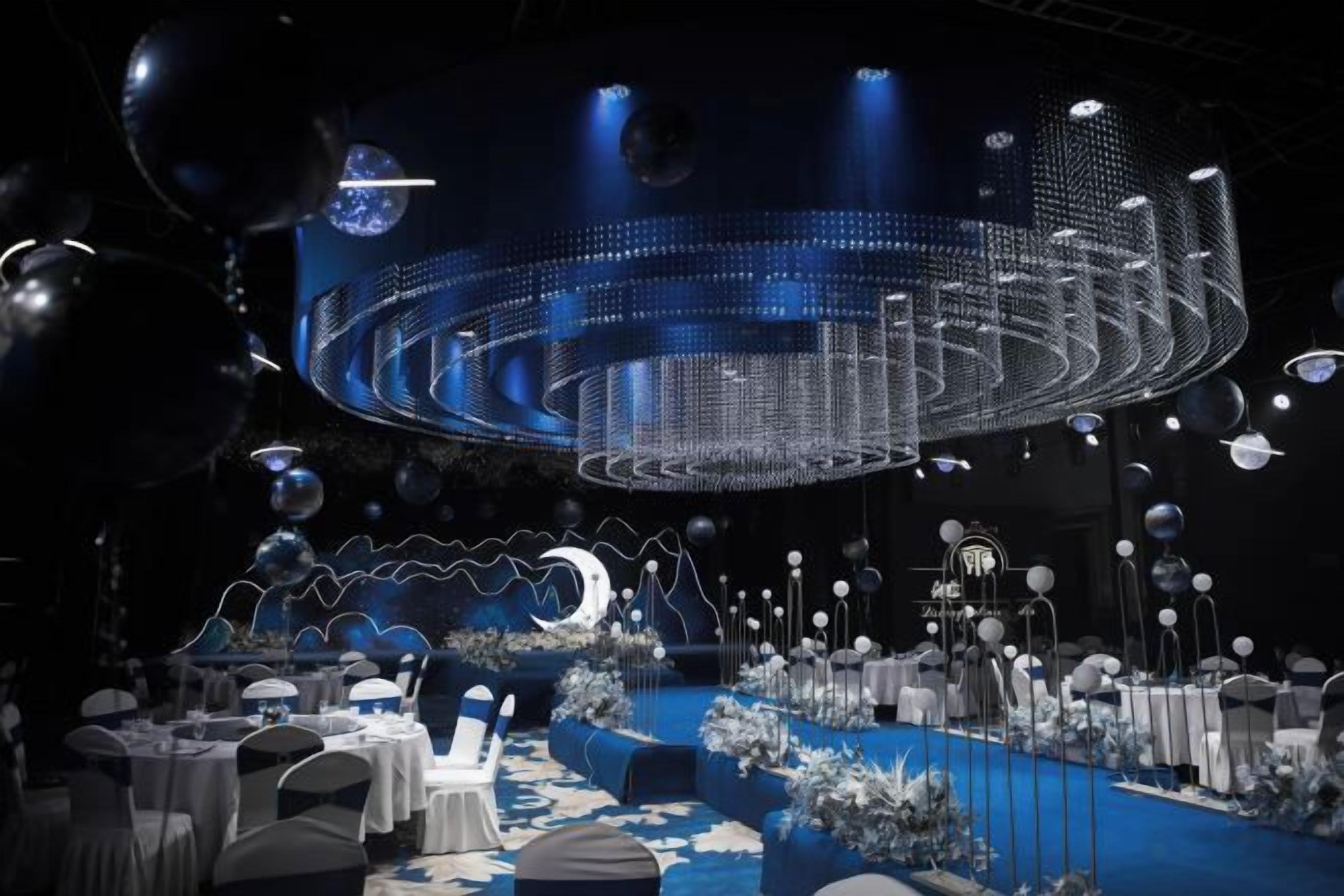 Une scène dotée d’une installation lumineuse circulaire, de tables avec des chaises et d’un tapis bleu.
