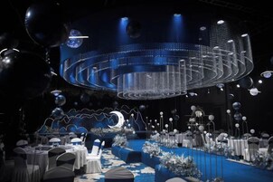 Un escenario con una instalación de luces circulares, mesas con sillas y una alfombra azul.