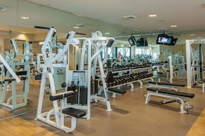 Une salle de sport équipée de divers appareils d’exercice, d’haltères et d’un écran de télévision.