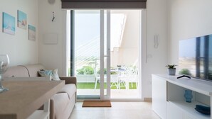 Een moderne woonkamer met een bank, een salontafel, een televisie en een schuifpui naar een balkon.