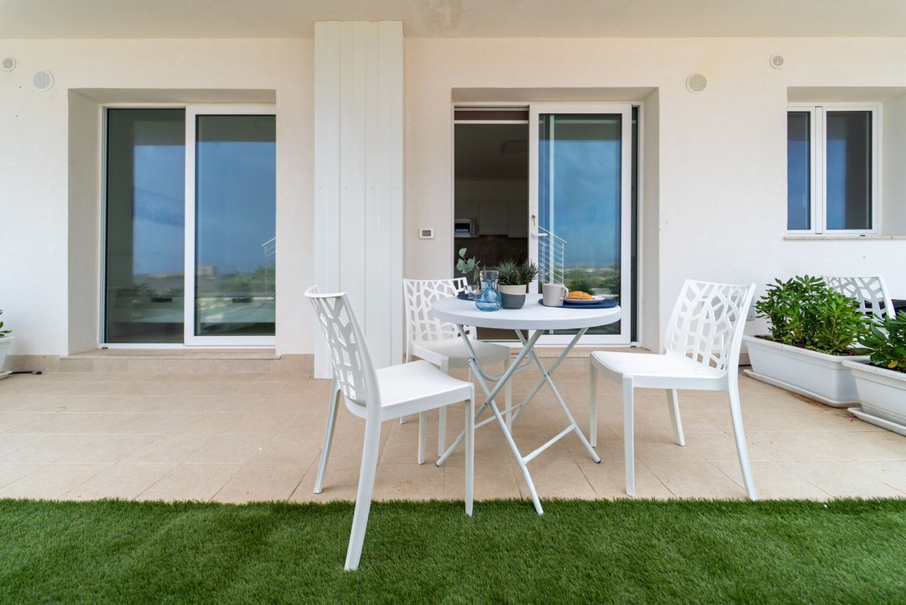 A patio with a round table and white chairs, a sliding glass door, and a view of the city.