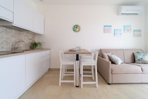 Una cocina moderna con armarios blancos, una mesa de comedor con sillas, un sofá color beige y un aire acondicionado instalado en la pared.