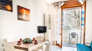 Ein Essbereich mit einem Tisch für zwei Personen, einem an der Wand montierten Fernseher und Blick ins Freie durch eine Glastür.
