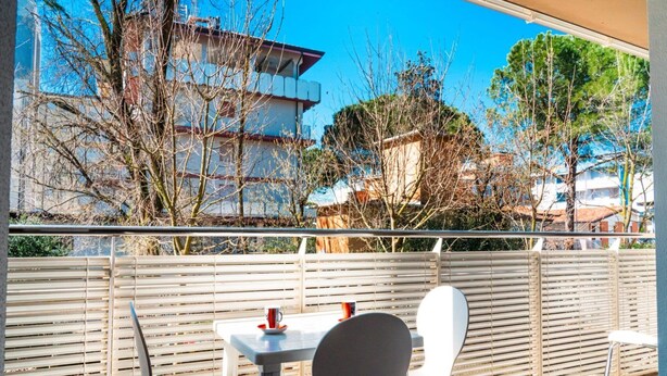 A balcony with a table and chairs, overlooking a residential area with trees and buildings. - A Lovely Modern Flat a Stone Throw From the sea (San Michele al Tagliamento)