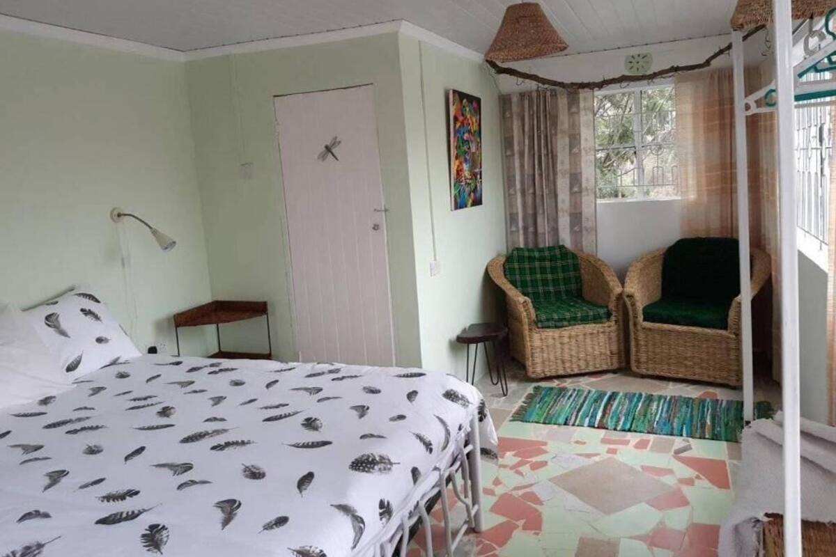 Une pièce comprenant un lit, une chaise, une petite table, une porte et une fenêtre avec des rideaux.