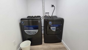 Twee Midea wasmachines in een smalle gang, met een witte emmer en een stopcontact op de muur.