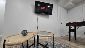 Een kamer met een wandgemonteerde televisie waarop 'NETFLIX' staat, een houten tafel met een helm, en een 'QUIKSET' bord.