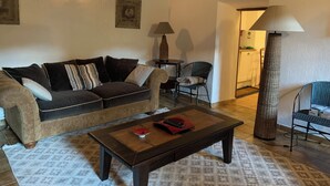 A cozy living room with a sofa, a coffee table, and a lamp. There is a cat tree and a chair in the corner.