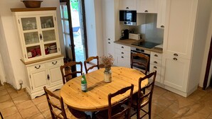 A kitchen with white cabinets, a wooden dining table, and chairs. There is a microwave, a coffee maker, and a window with curtains.