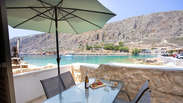 A glass table with chairs and an umbrella, overlooking a coastal area with a boat and buildings. - Captain Antonis - Authentic Seafront Living in Gerolimenas (Gerolimenas)