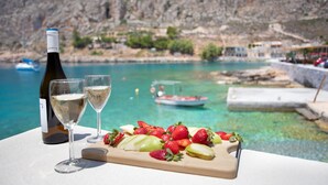 A table with a bottle of wine, two glasses, and a fruit platter by a pool with a rocky backdrop. - Captain Antonis - Authentic Seafront Living in Gerolimenas (Gerolimenas)