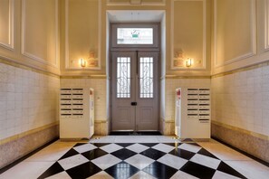 A hotel lobby with a checkered floor, a double door with a window, and a wall-mounted elevator control panel.