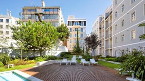 Un moderno complejo de apartamentos con piscina en la azotea, mobiliario de exterior y abundante vegetación.