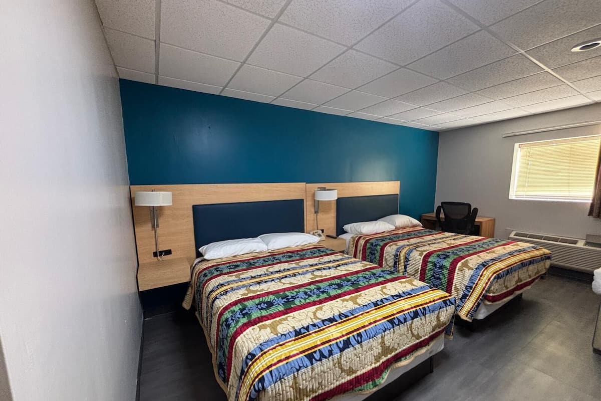 A hotel room with two beds, each with a patterned bedspread, a wooden headboard, and bedside lamps.