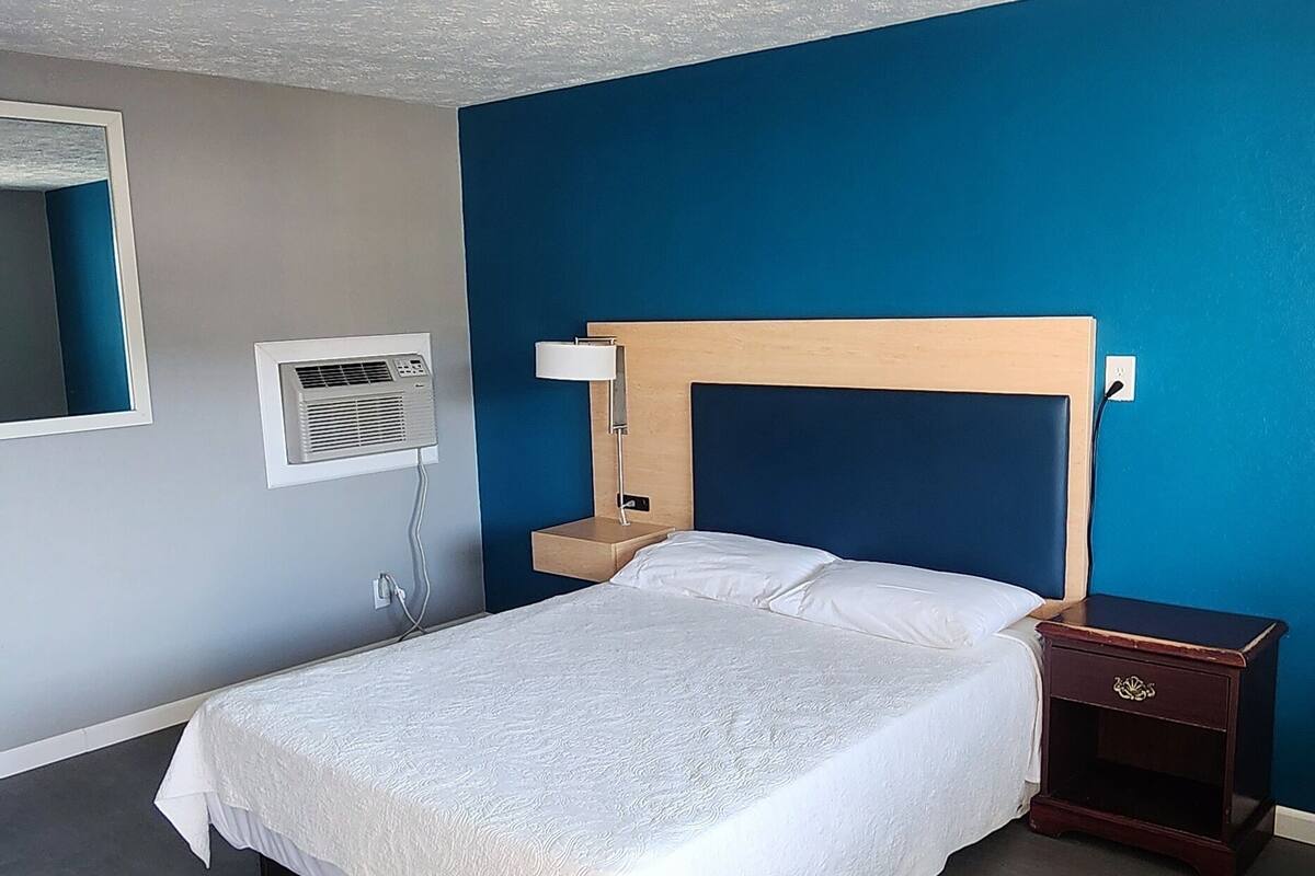 A bedroom with a bed, bedside table, and a wall-mounted air conditioning unit.