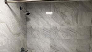 Un área de ducha con puerta de vidrio, cabezal de ducha de metal y barra de apoyo metálica.